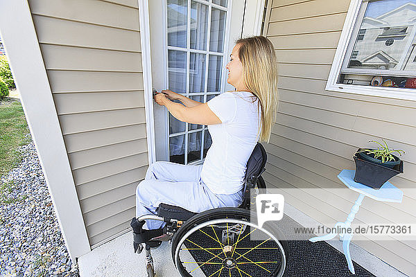 Frau im Rollstuhl verschließt die Haustür ihres Hauses