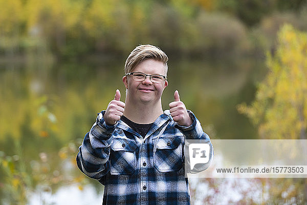 A young man with Down Syndrome giving a thumbs up in a city park on a warm fall evening: Edmonton  Alberta  Canada