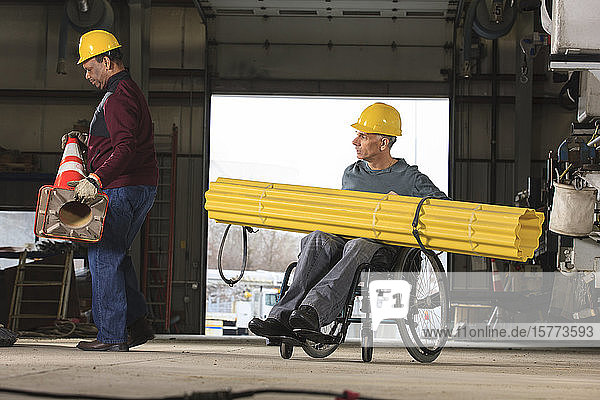 Ein behinderter Arbeiter und ein Kollege transportieren Material in einer Werkstatt