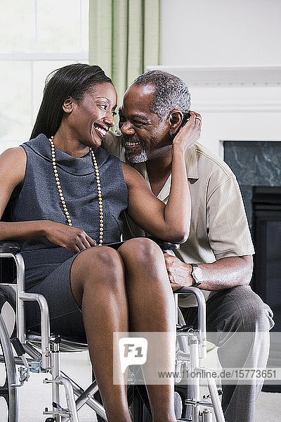 Ein Mann mittleren Alters turtelt mit einer Frau mittleren Alters  die im Rollstuhl sitzt und lächelt