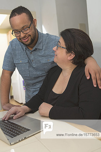 Mutter und junger erwachsener Sohn benutzen zu Hause einen Laptop