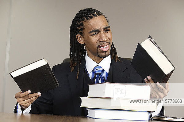 Ein verwirrter junger Geschäftsmann hält Bücher in einem Büro.