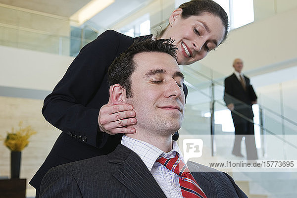 Blick auf eine Geschäftsfrau  die einer Führungskraft in einem Büro eine Massage gibt.