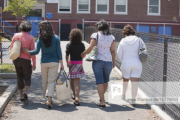 Eine Gruppe von Frauen aus drei Generationen  die gemeinsam in einer Reihe auf einem Gehweg im Freien gehen