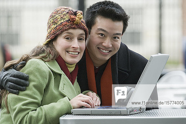 Porträt eines jungen Paares mit einem Laptop in einem Straßencafé