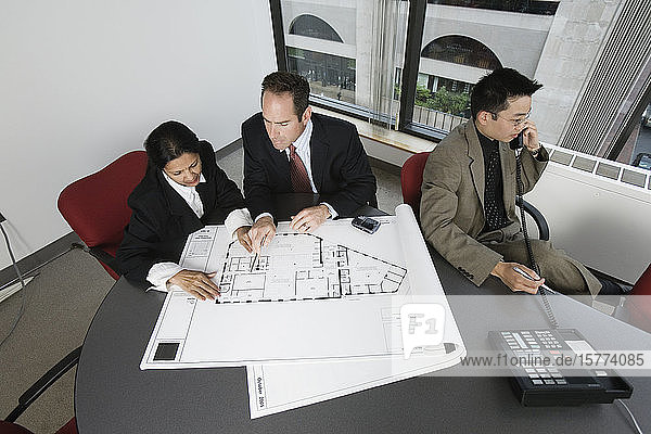 Blick auf Geschäftsleute  die einen Bauplan prüfen  während ein Architekt am Telefon spricht.