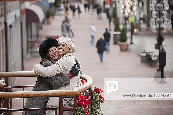 Zwei Frauen umarmen sich  während sie auf einem weihnachtlich geschmückten Balkon stehen und auf die Stadt hinausschauen; Boston  Massachusetts  Vereinigte Staaten von Amerika