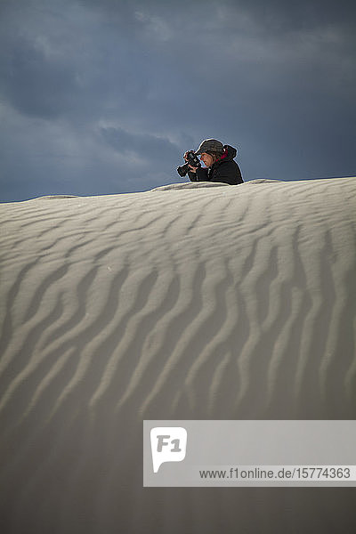Female photographer takes a picture with white sand in the foreground White Sands National Monument; Alamogordo New Mexico United States of America