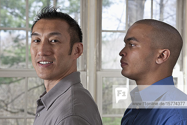 Portrait of the side view of two young businessmen standing facing left  one looking at the camera
