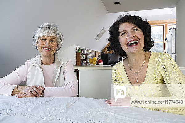 Zwei fröhliche Frauen sitzen an einem Esstisch.