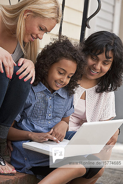 Ein junges Mädchen benutzt einen Laptop  während ihre Mutter und eine junge Frau zusehen