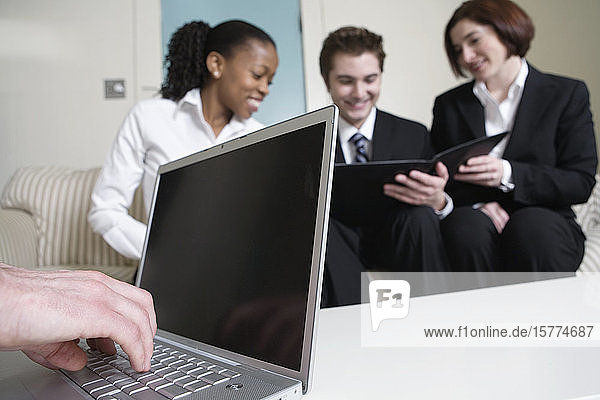 Nahaufnahme einer Hand  die an einem Laptop arbeitet  mit Geschäftsleuten im Hintergrund.