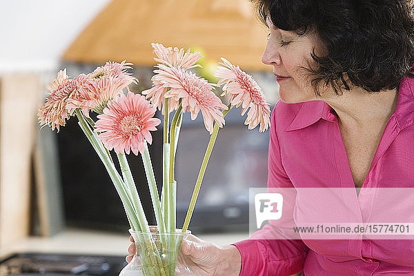 Eine Frau  die an rosa Gänseblümchen riecht.