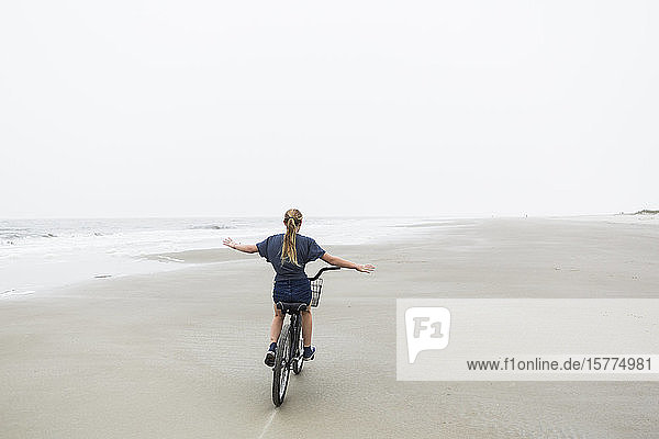 Ein junges Mädchen mit dem Fahrrad an einem Sandstrand am Meer
