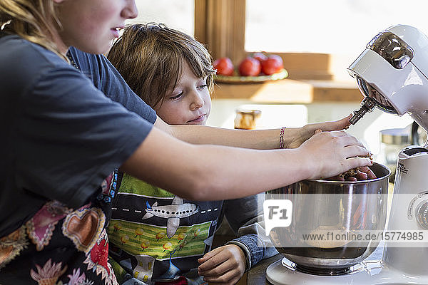 Ein junges Mädchen und ihr 6-jähriger Bruder in einer Küche  mit einer Rührschüssel