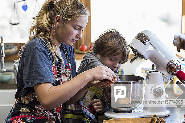 Ein junges Mädchen und ihr 6-jähriger Bruder in einer Küche  mit einer Rührschüssel