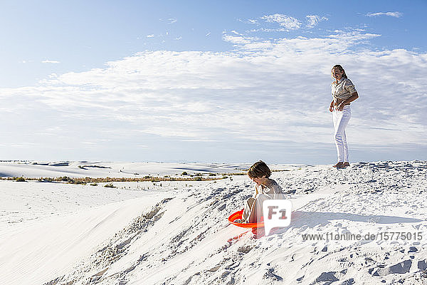 Children playing in sand dunes landscape  one on an orange sled.