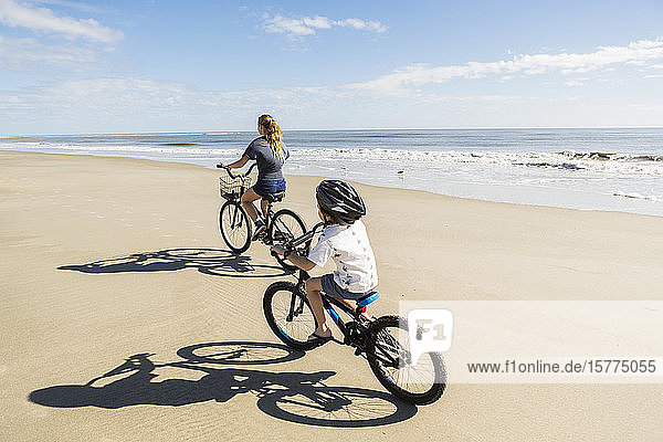 Kinder  die auf dem Sand am Wasser Fahrrad fahren  ein Junge und ein Mädchen.