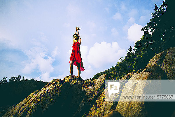 Tiefblick auf eine junge Frau in rotem Kleid  die auf Felsen steht.