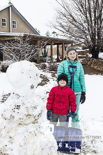 A teenage girl and her 6 year old brother posing with snowman