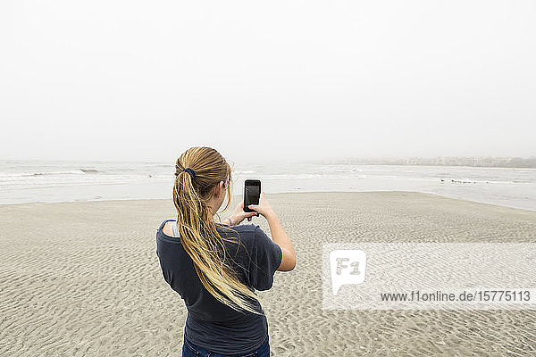Ein Teenager  der am Strand mit einem Smartphone Bilder spricht