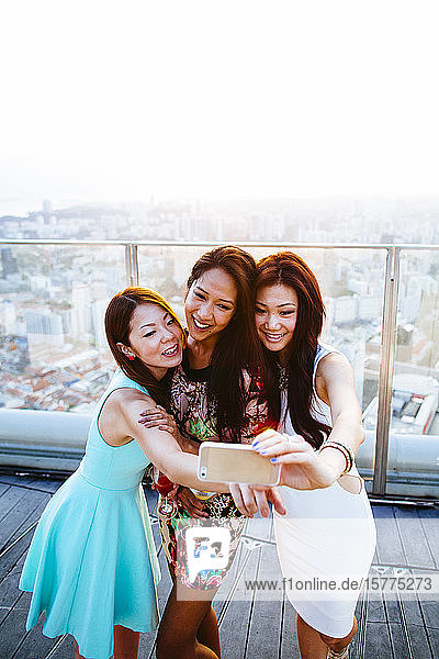 Drei Frauen  die auf einem Dach in Singapur stehen und Selfie mit dem Handy nehmen.