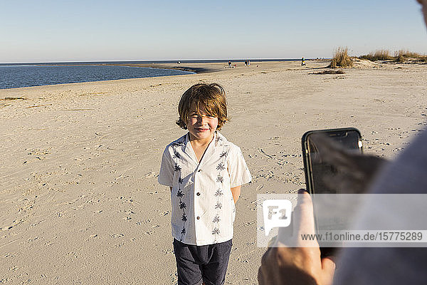 A six year old boy being photographed by his mother at the beach