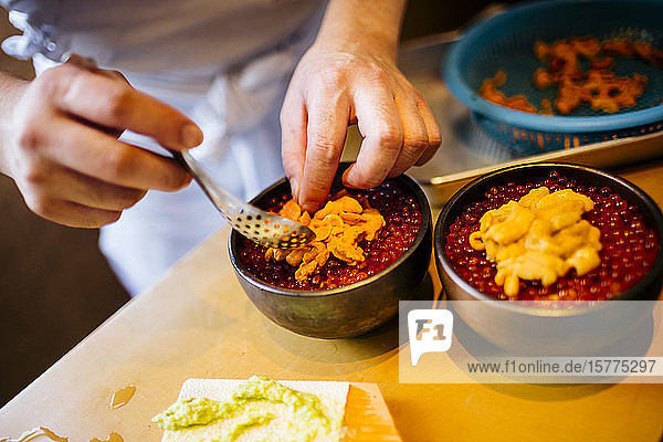 Nahaufnahme des Küchenchefs bei der Zubereitung von Uni  Seeigel  mit Lachsrogen und Reis.