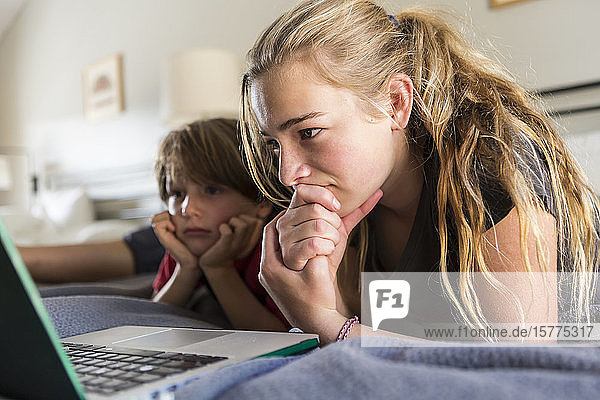 13-jährige Schwester und ihr Bruder betrachten Laptop auf dem Bett