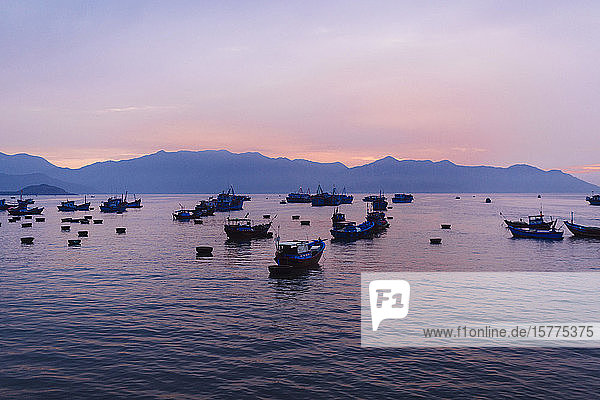 Große Gruppe von Fischern in traditionellen Fischerbooten bei Sonnenaufgang auf dem See  Berge in der Ferne.