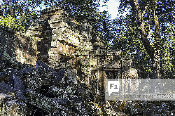 Ankor Wat  ein historischer Khmer-Tempel aus dem 12. Jahrhundert und UNESCO-Weltkulturerbe. Bögen und geschnitzte Steinblöcke in Ruinen von Tempelpavillons  wobei Bäume die Gebäude dominieren.