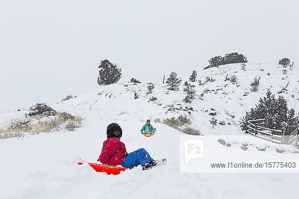 A boy and girl sledding down hill in snow