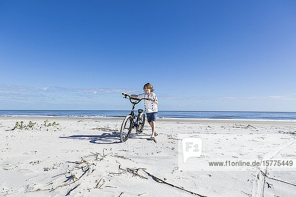 A young boy biking on a sandy beach