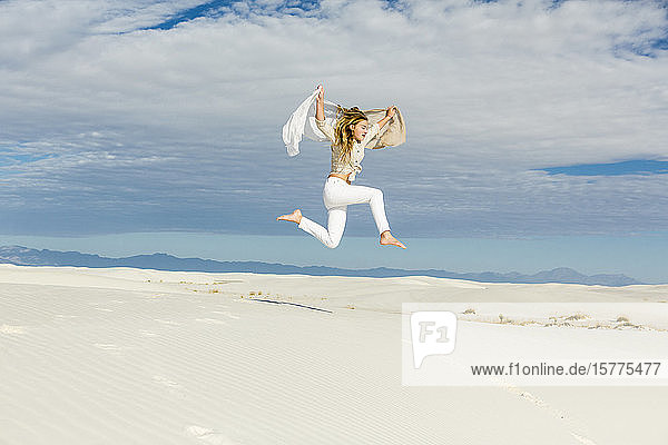 Ein Teenager-Mädchen tanzt und springt mitten in der Luft im offenen Raum auf weißen Sanddünen