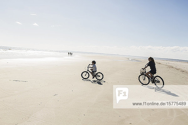 Zwei Kinder radeln an einem offenen Strand  ein Junge und ein Mädchen.