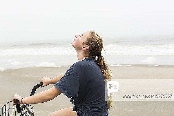 A teenage girl biking on sand on a beach