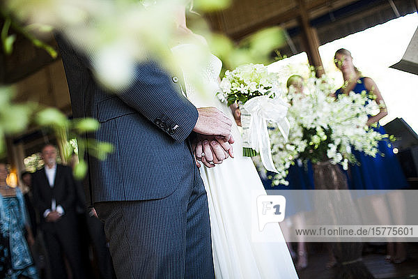 Close up of bride and groom holding hands at a wedding ceremony.