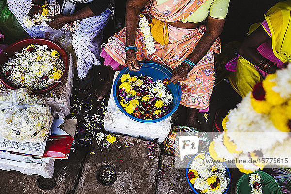 Nahaufnahme aus hoher Perspektive von Frauen  die auf einem Markt Blumen an Schnüren schnüren.