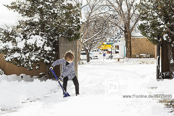 Ein kleiner Junge schaufelt Schnee in der Einfahrt