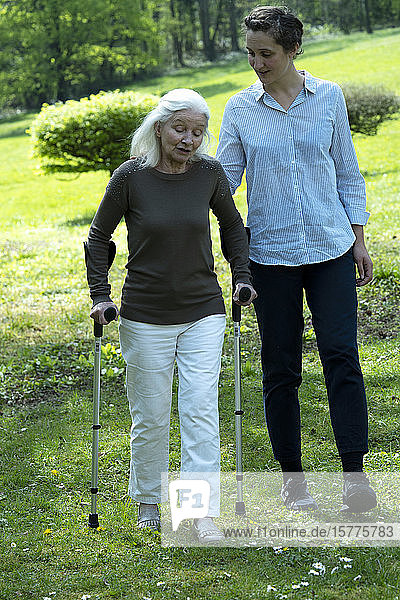 Pflegerin und ältere Frau gehen im Garten spazieren