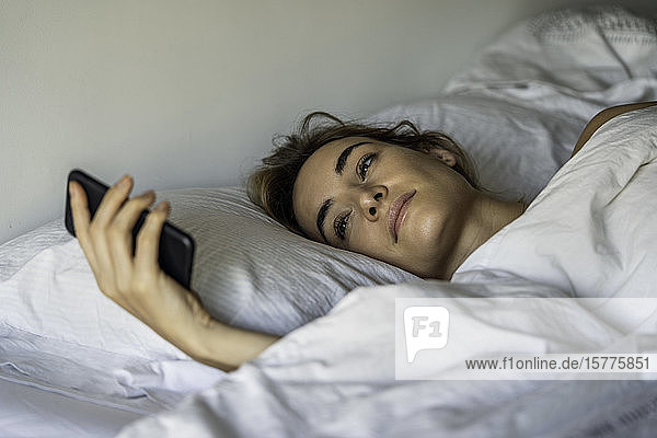 Junge Frau schaut auf dem Bett auf ihr Smartphone