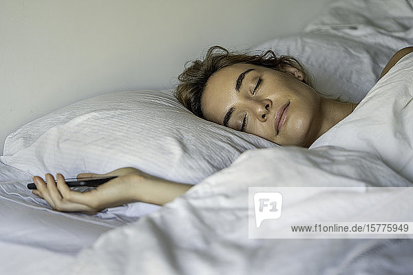 Junge Frau schläft mit Smartphone