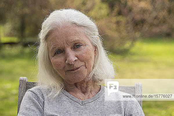 Porträt einer älteren Frau  die im Garten sitzt