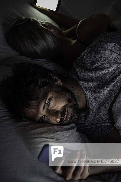 Junges Paar benutzt Smartphone auf dem Bett