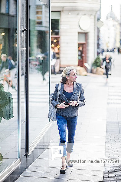 Eine reife Geschäftsfrau schaut weg  während sie an einem Bürogebäude vorbeigeht