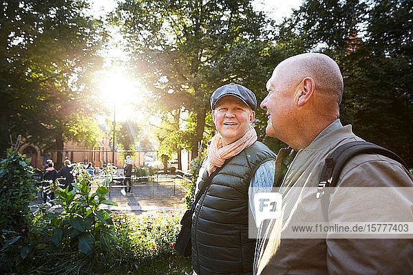 Lächelnder älterer Mann geht mit einem Freund im Park gegen Bäume in der Stadt