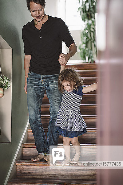 Father holding hands with daughter while climbing steps at home