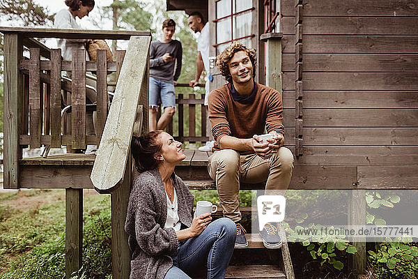 Smiling woman looking at man sitting on steps while friends standing in background