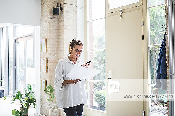 Female designer talking through smart phone while looking at document in home office