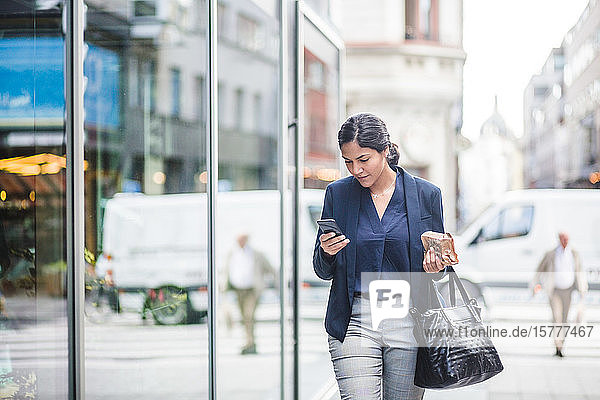 Geschäftsfrau benutzt Telefon im Vorbeigehen am Gebäude